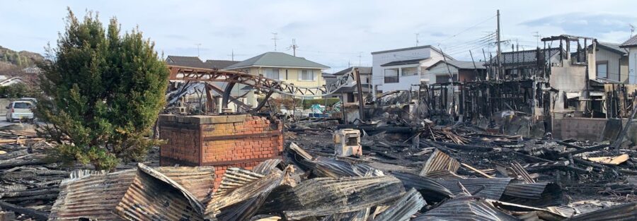 A neighborhood where half the houses are standing and the other half have been burned down to charred ruins.