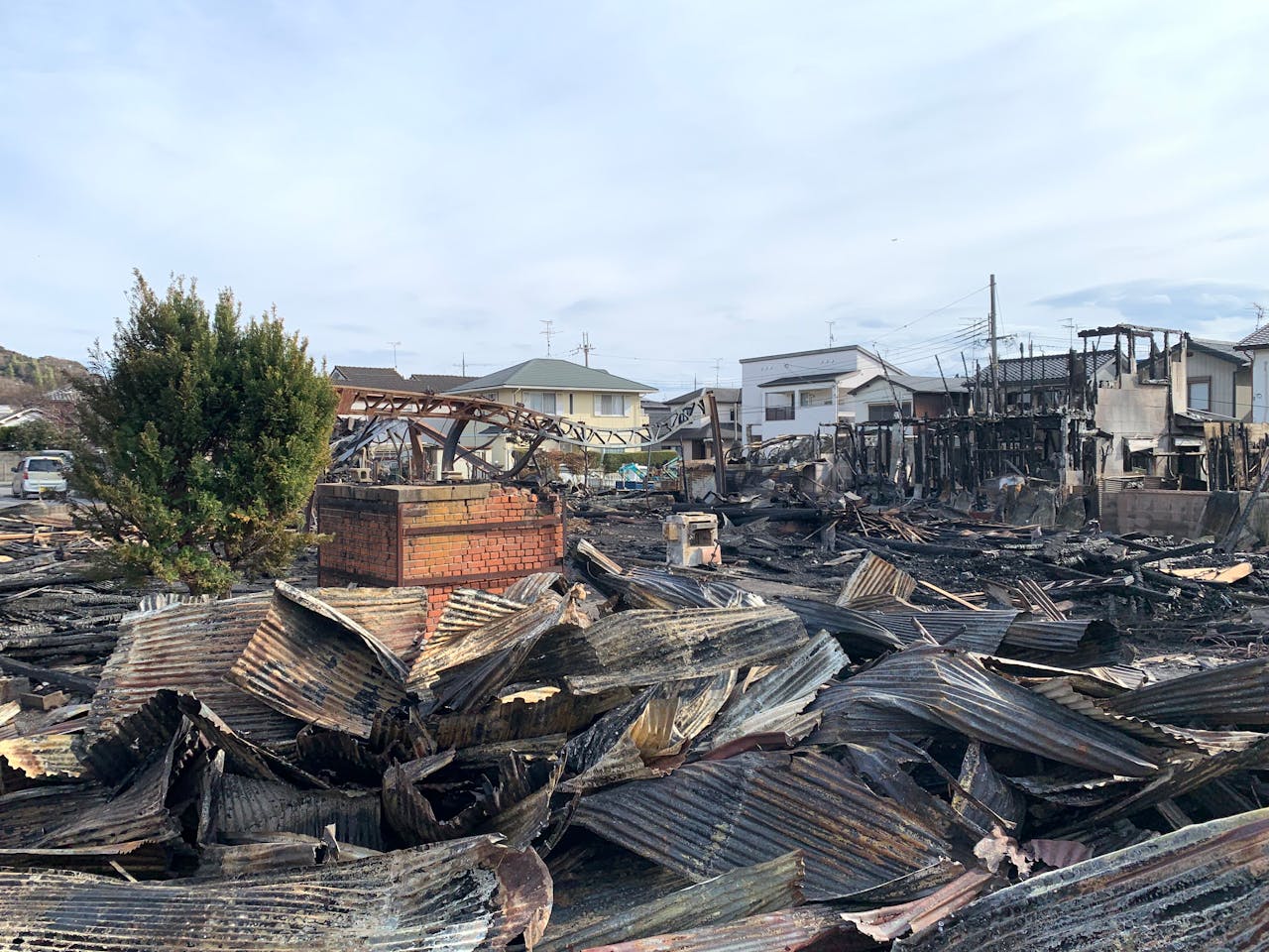 A neighborhood where half the houses are standing and the other half have been burned down to charred ruins.
