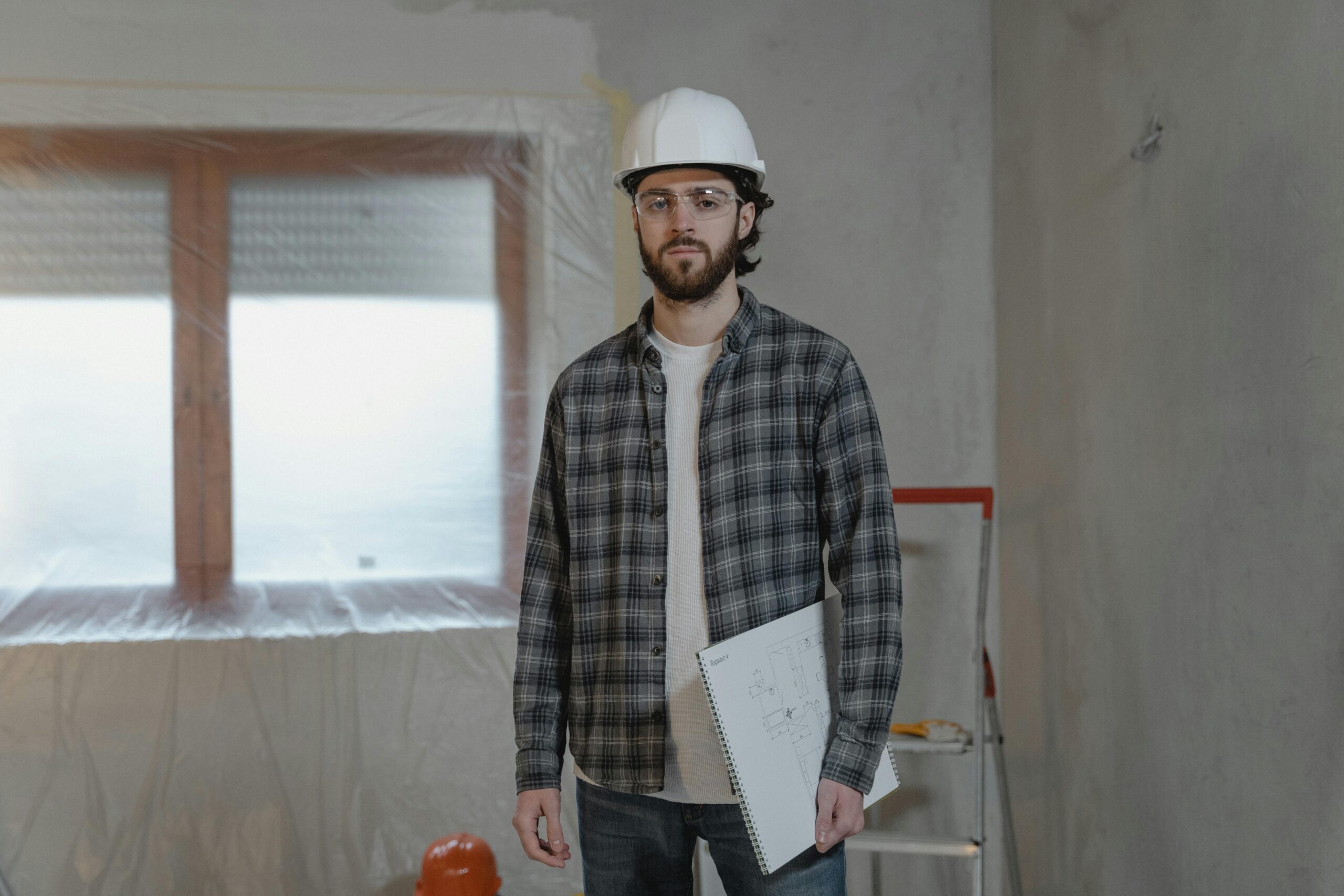 Contractor wearing safety gear and holding blueprints while inspecting storm damage repairs inside a California home.